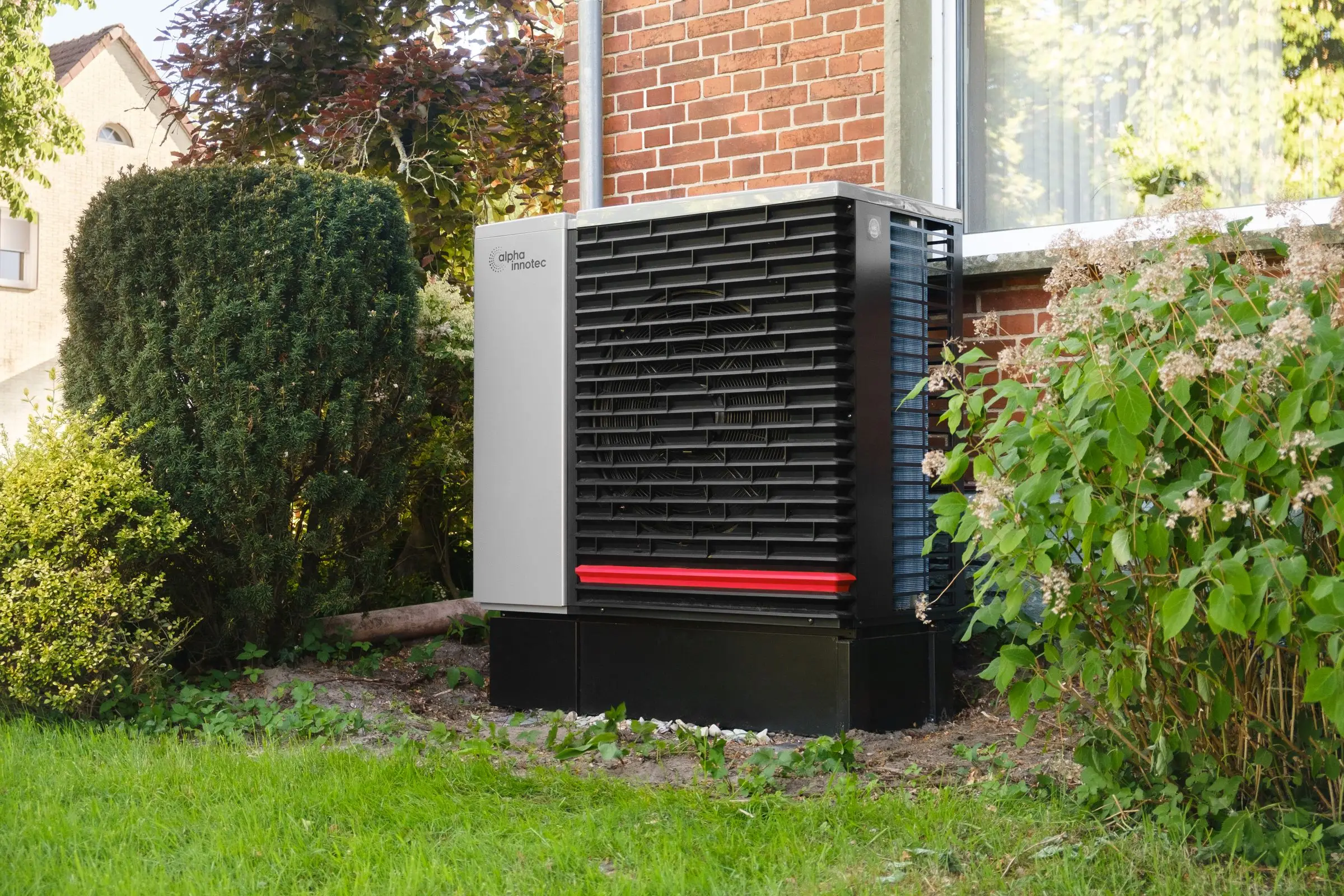 Außeneinheit einer Wärmepumpe vor einem Klinkerhaus im Garten